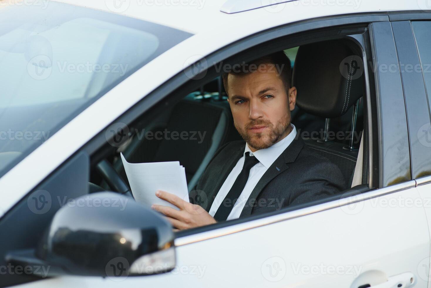 Always in a hurry. Handsome young man in full suit smiling while driving a car. photo