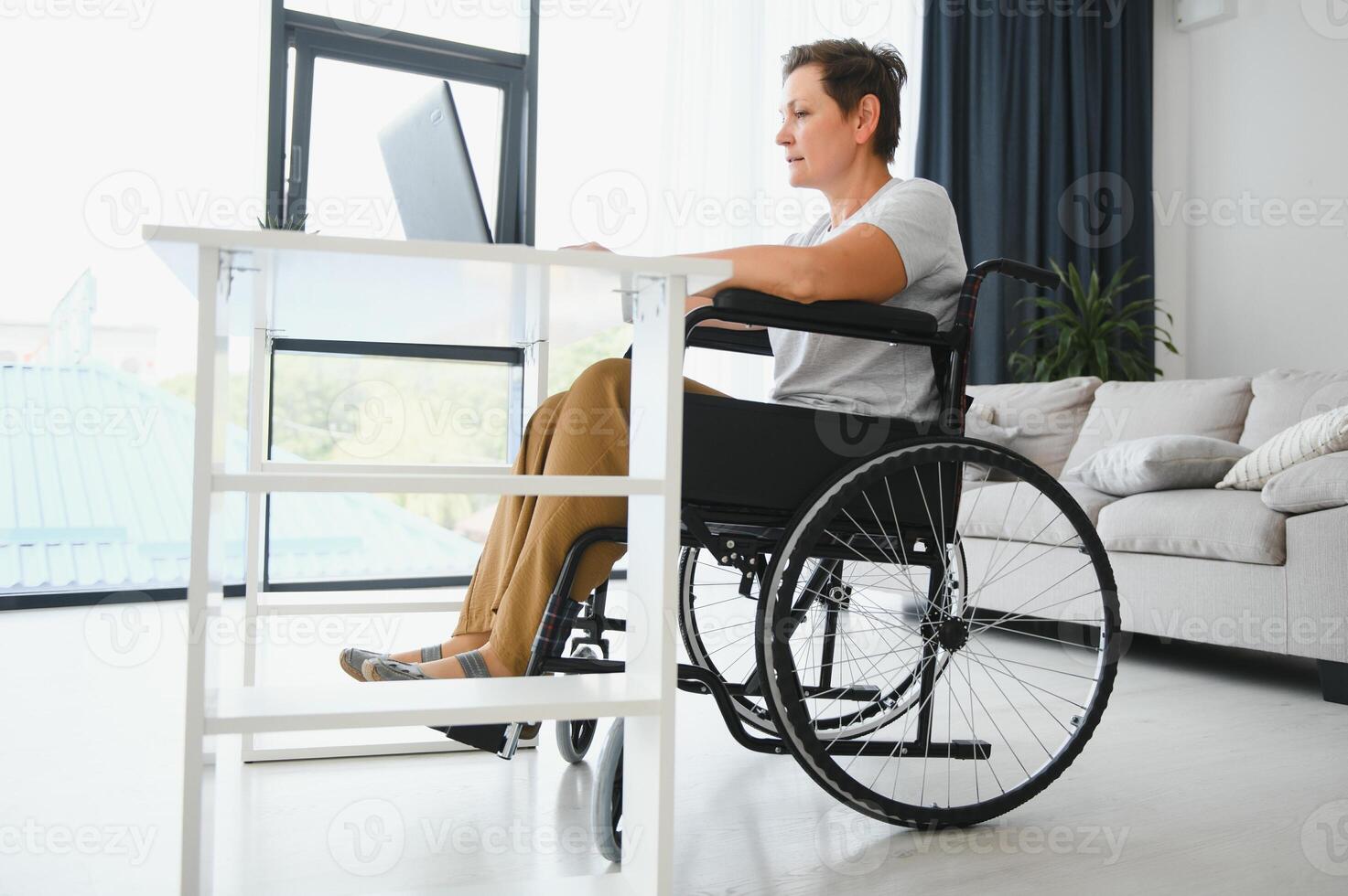 positivo mayor mujer en silla de ruedas trabajando en computadora portátil, eso persona de libre dedicación, en línea foto