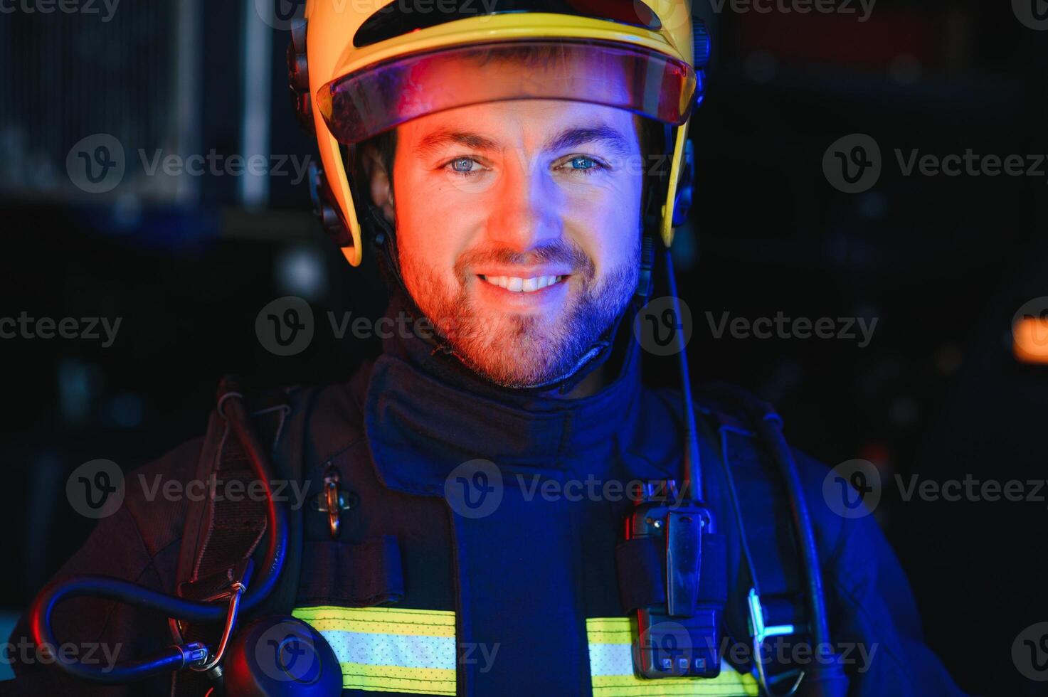 Confident fireman wearing protective uniform standing next to a fire engine in a garage of a fire department photo