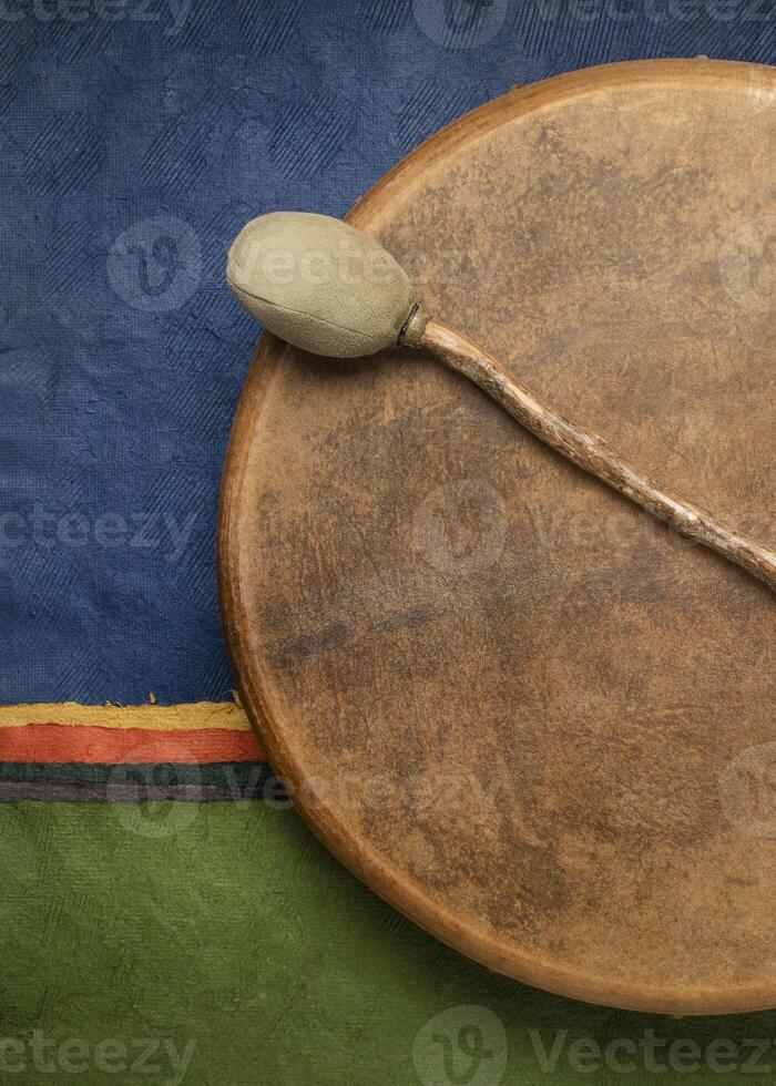 handmade, native American style, shaman frame drum covered by goat skin with a beater against colorful abstract paper landscape photo