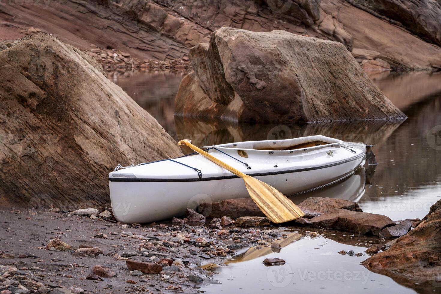 decked expedition canoe with a wooden paddle on a rocky shore of Horsetooth Reservoir near Fort Collins, Colorado, low water level fall or winter scenery photo