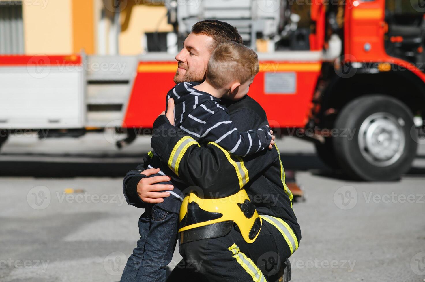 Dirty firefighter in uniform holding little saved boy standing on black background. photo