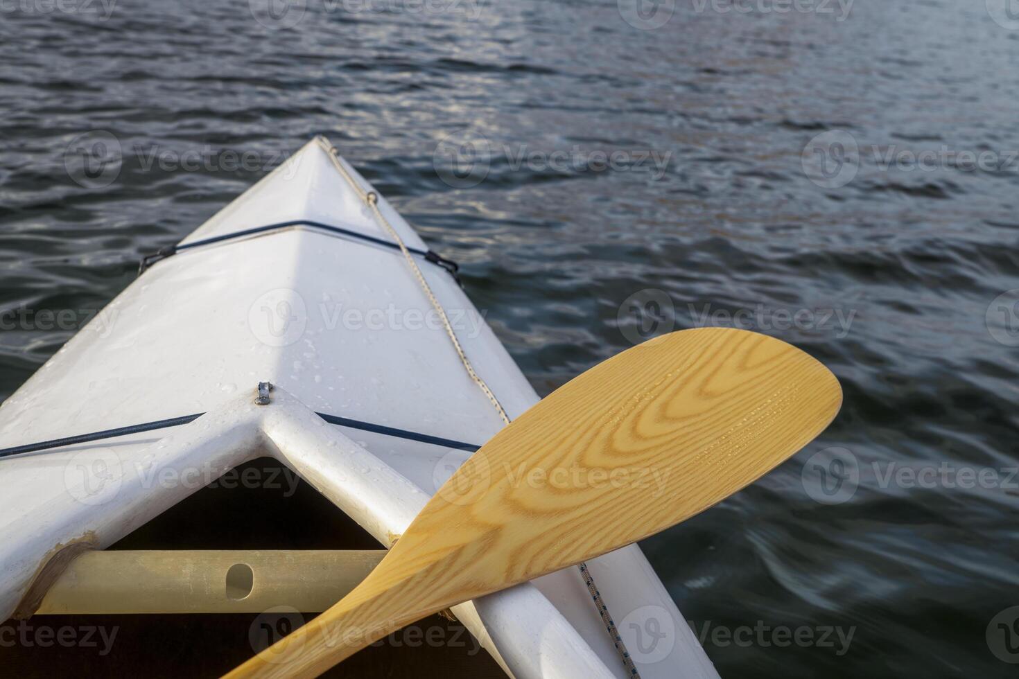 bow of a decked expedition canoe with wooden paddle on a lake, paddler view photo