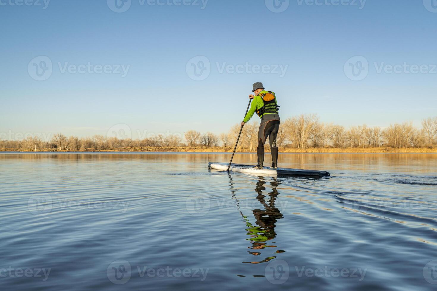 senior male paddler is paddling stand up paddleboard on a calm lake in early spring scenery in Colorado photo