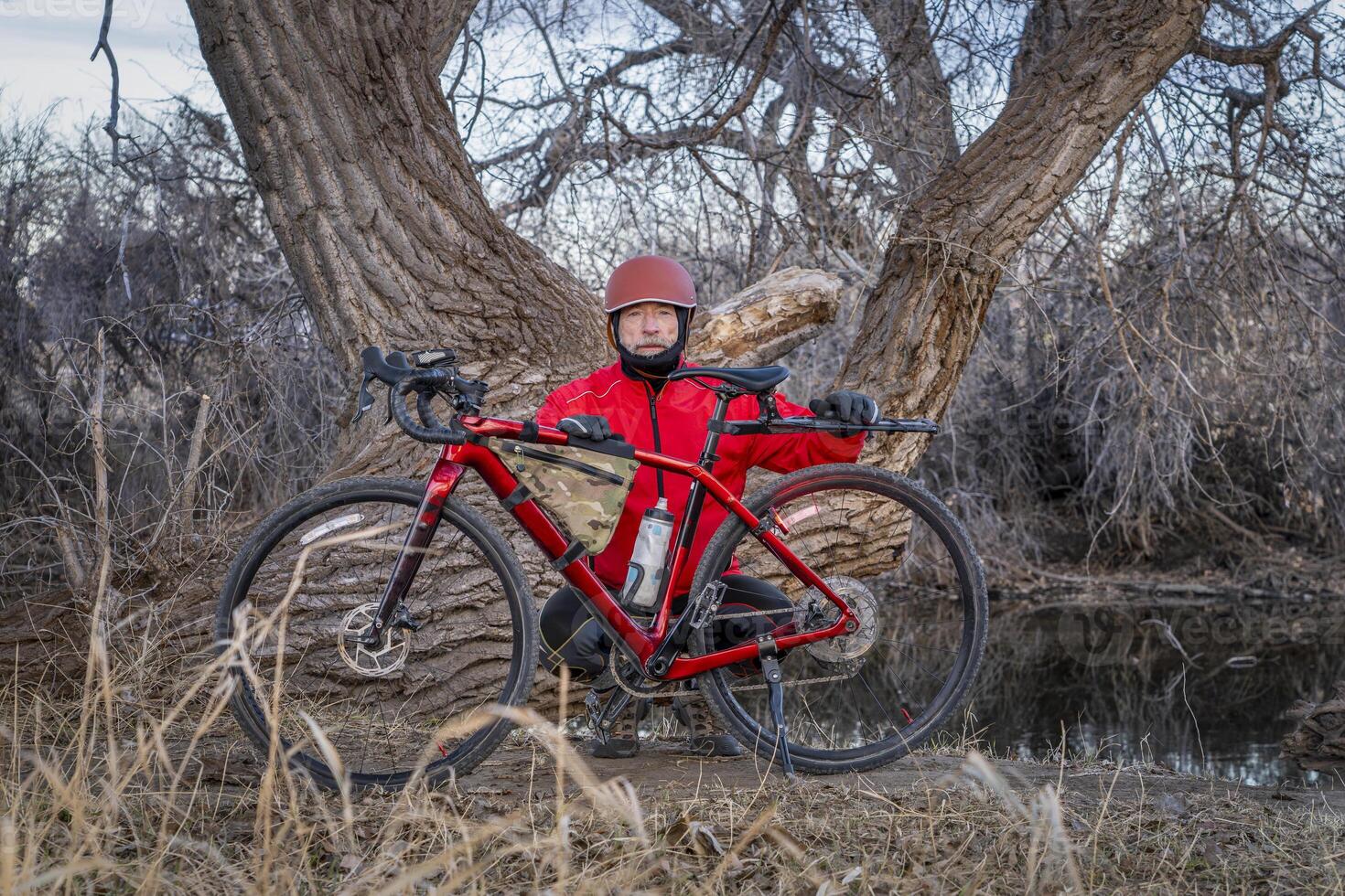 senior male cyclist with a gravel bike on a shore of the Poudre River in northern Colorado in winter scenery photo