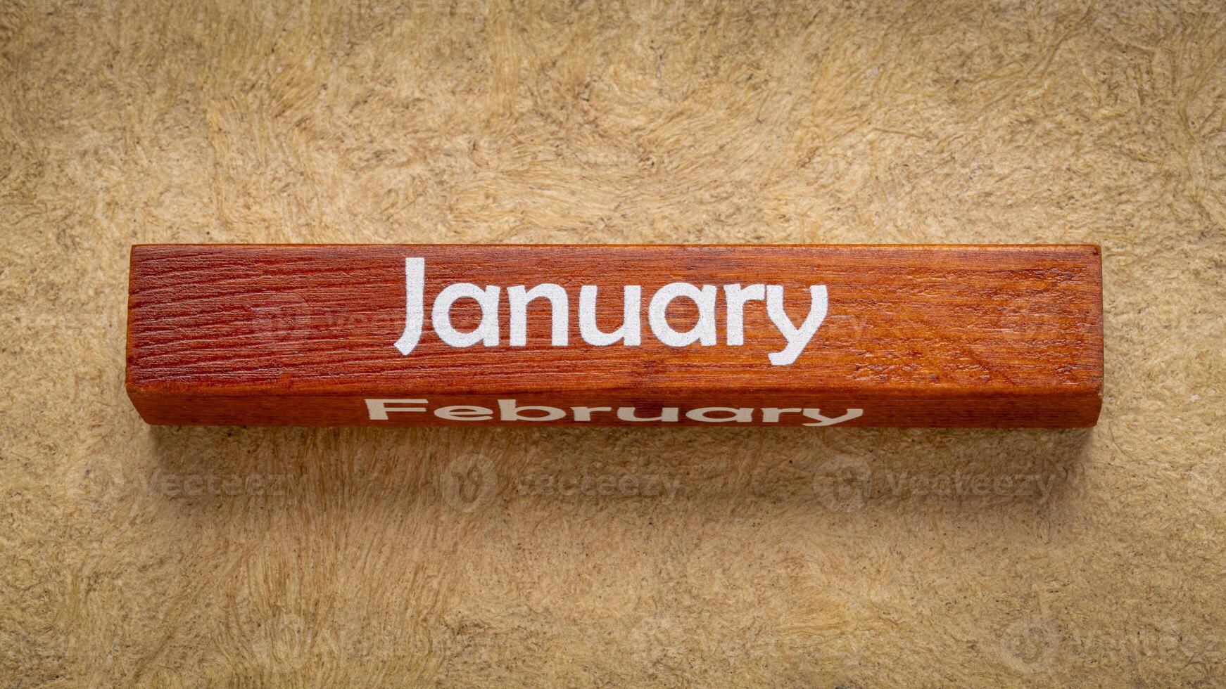 January and February text on wooden block against handmade bark paper in earth tones, calendar concept photo