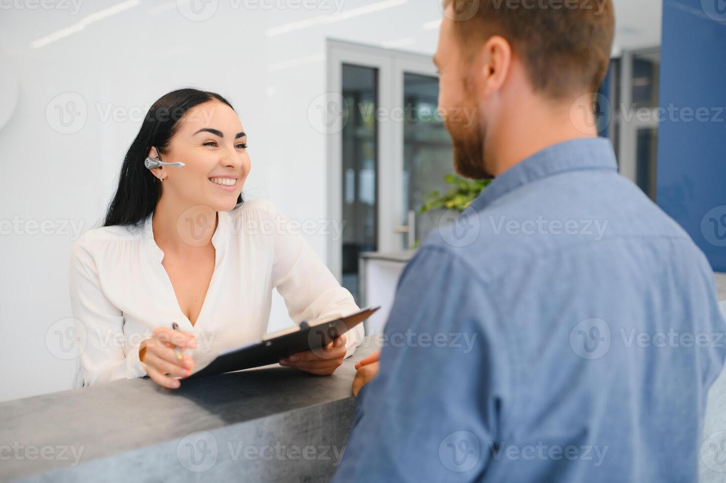 The employee of the beauty salon meets the client in the reception of a modern beauty salon. A man signs a paper with the consent for maintenance. The woman smiles at him photo