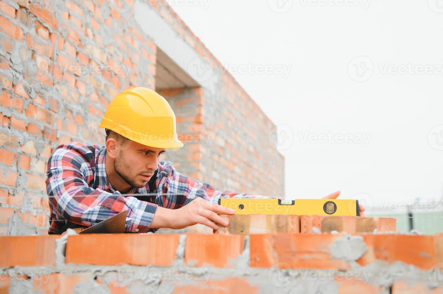 Using bricks. Young construction worker in uniform is busy at the unfinished building photo