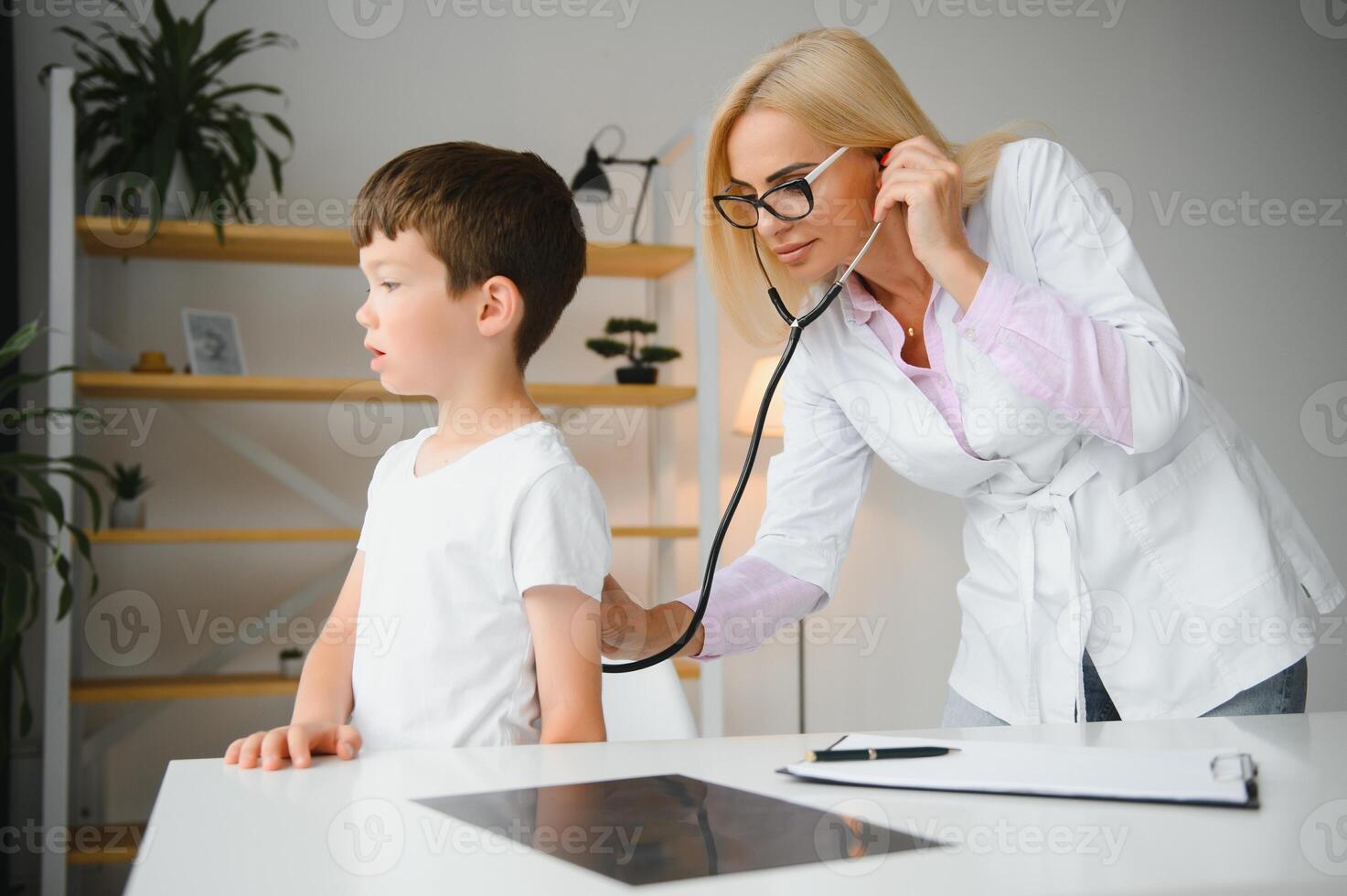 Pediatrician doctor examining little boy's heart beat and lungs to check for problems photo