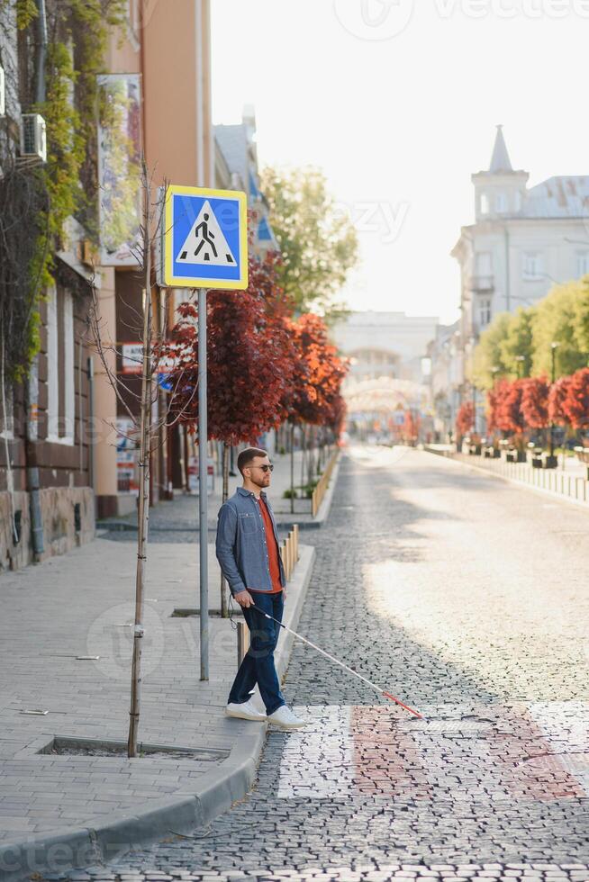 Young handsome blinded man walking with stick in town photo
