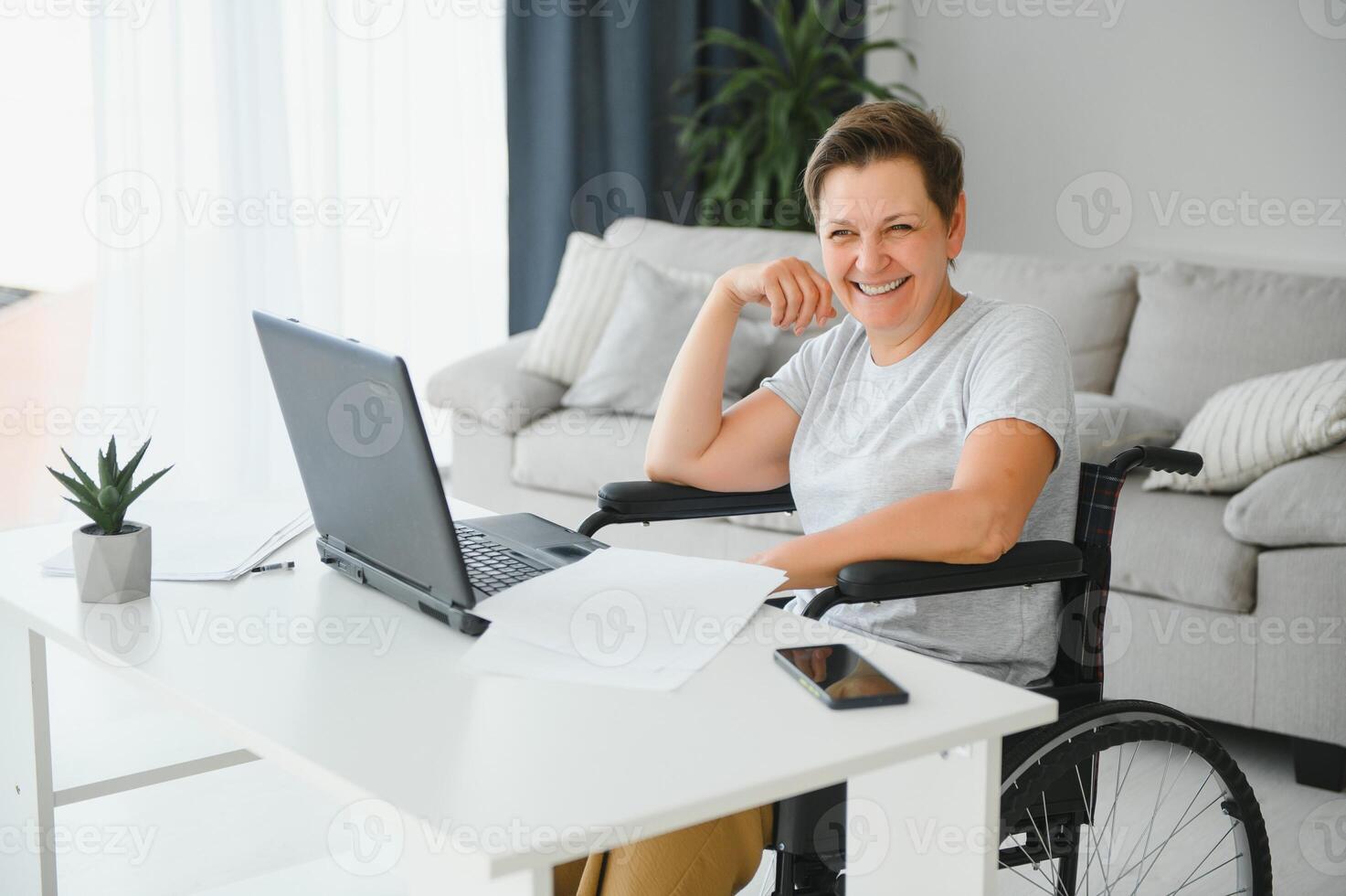 Freelancer in wheelchair using laptop near notebook and papers on table photo