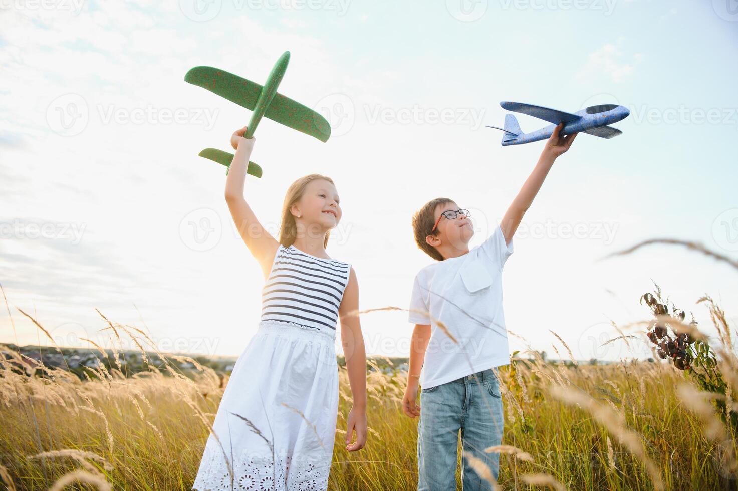 Running boy and girl holding two green and blue airplanes toy in the field during summer sunny day photo