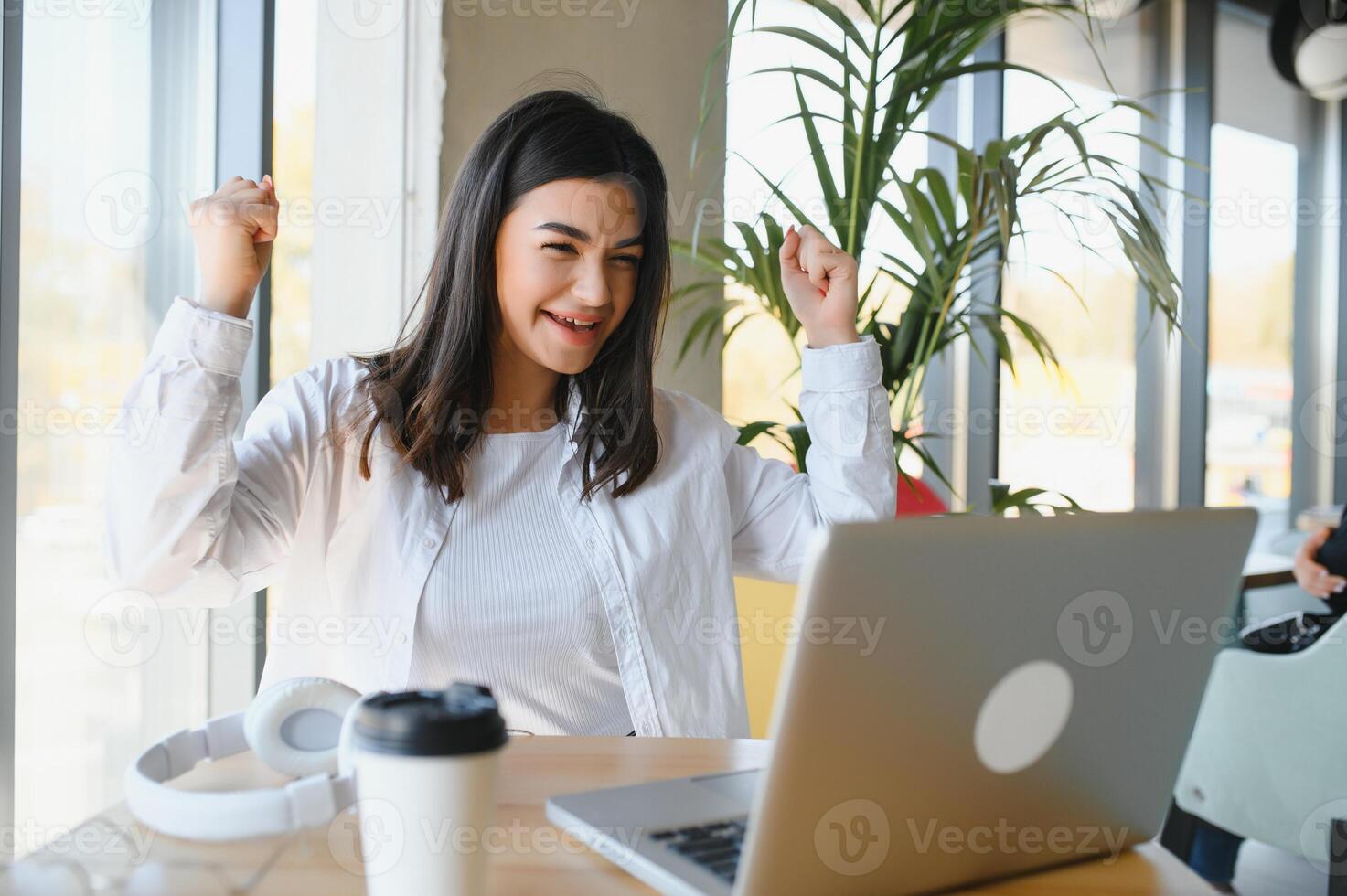 niña se regocija en victorioso teniendo elevado su manos arriba sentado en frente de laptop.chica sentado en cafetería, relojes en línea Deportes partido en computadora. foto