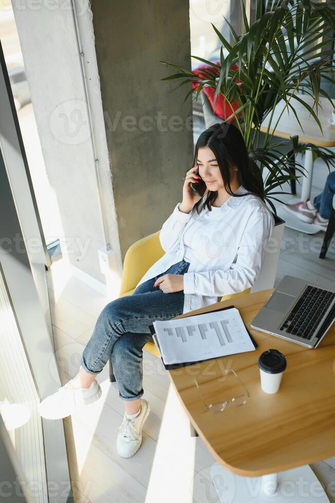 Beautiful Young Freelancer Woman Using Laptop Computer Sitting At Cafe Table. Happy Smiling Girl Working Online Or Studying And Learning While Using Notebook. Freelance Work, Business People Concept. photo