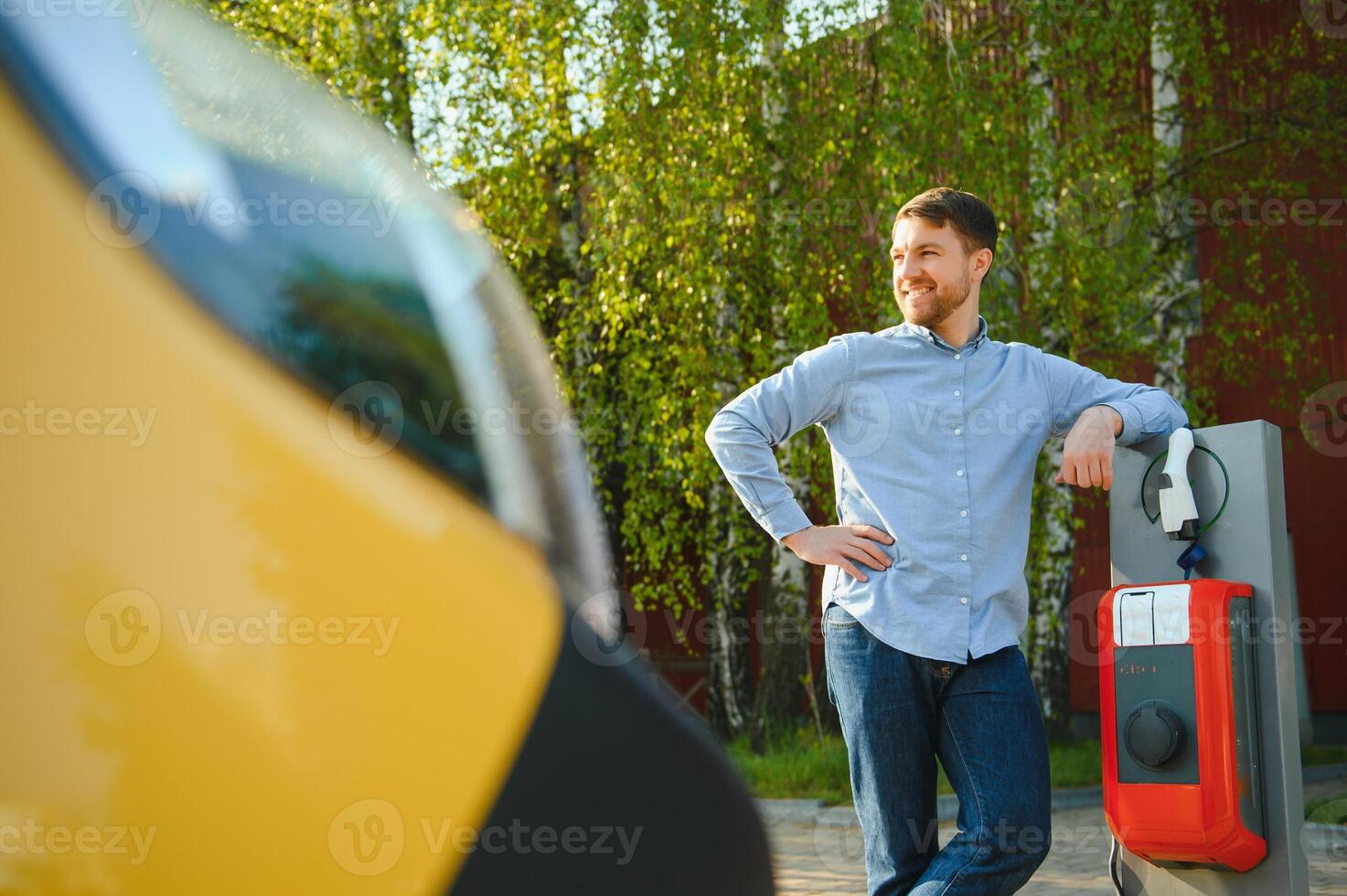 Portrait of a young man standing with charging cable near the charging station. Concept of fast home car chargers photo