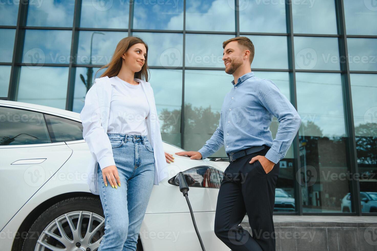 Young couple man and woman traveling together by new car having stop at charging station. photo