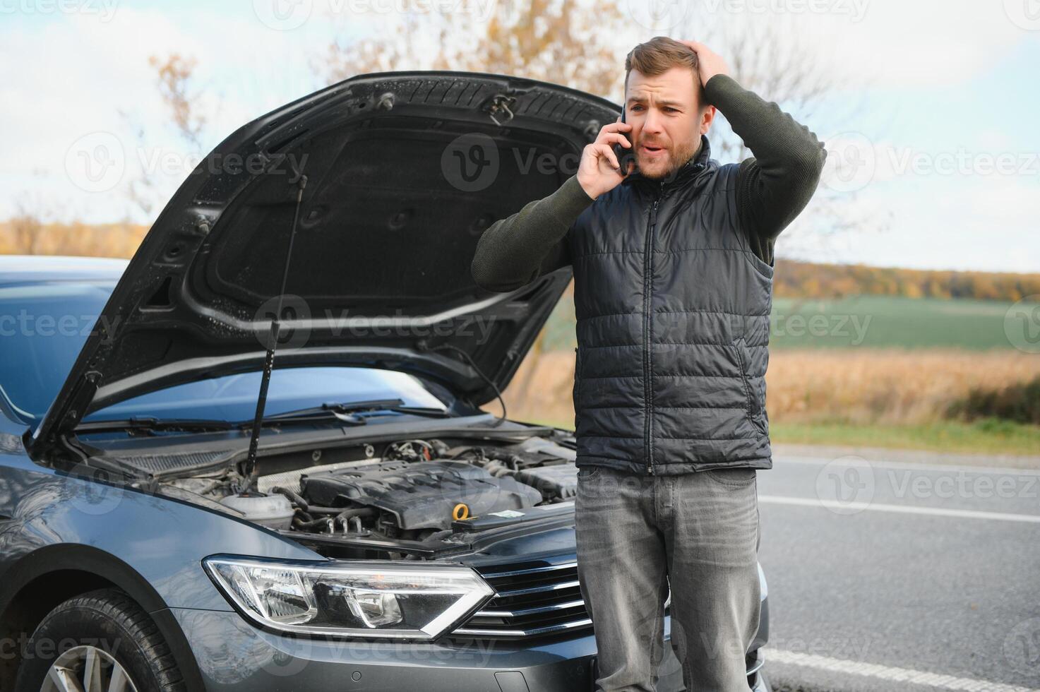 Handsome young man calling for assistance with his car broken down by the roadside photo