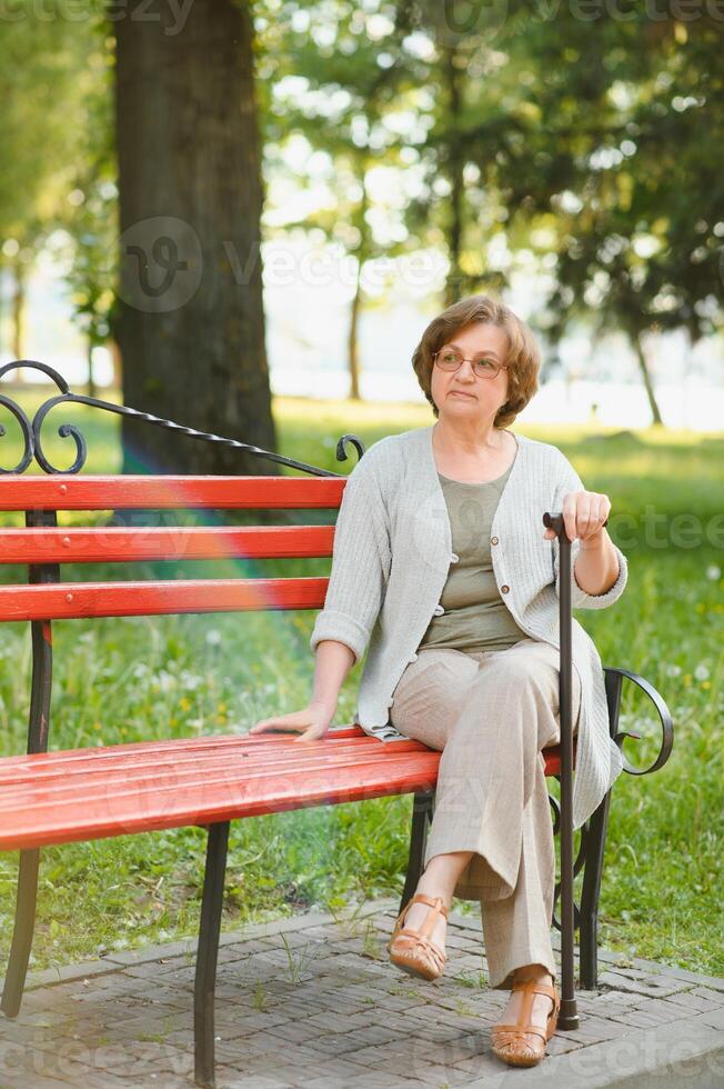 Elderly woman sitting and relaxing on a bench outdoors in park photo