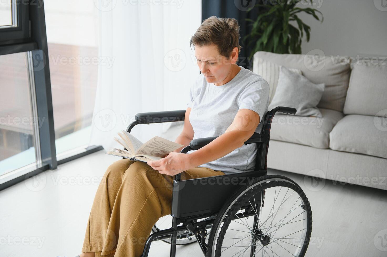 Shot of a senior woman sitting in a wheelchair and reading book at home photo