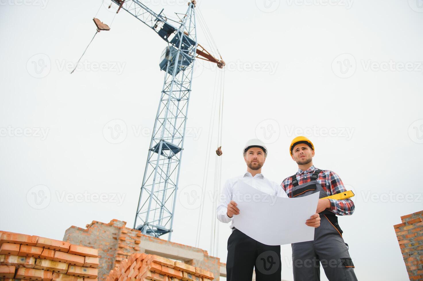 Construction engineers supervising progress of construction project stand on new concrete floor top roof and crane background. photo