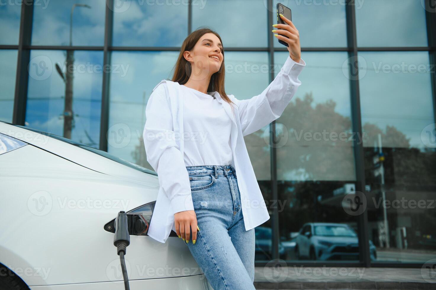 mujer con teléfono cerca un alquiler eléctrico coche. vehículo cargado a el cargando estación foto