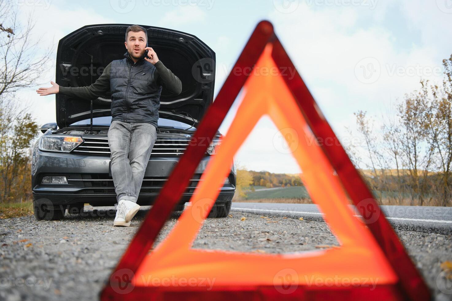 Man repairing a broken car by the road. Man having trouble with his broken car on the highway roadside. Man looking under the car hood. Car breaks down on the autobahn. Roadside assistance concept. photo