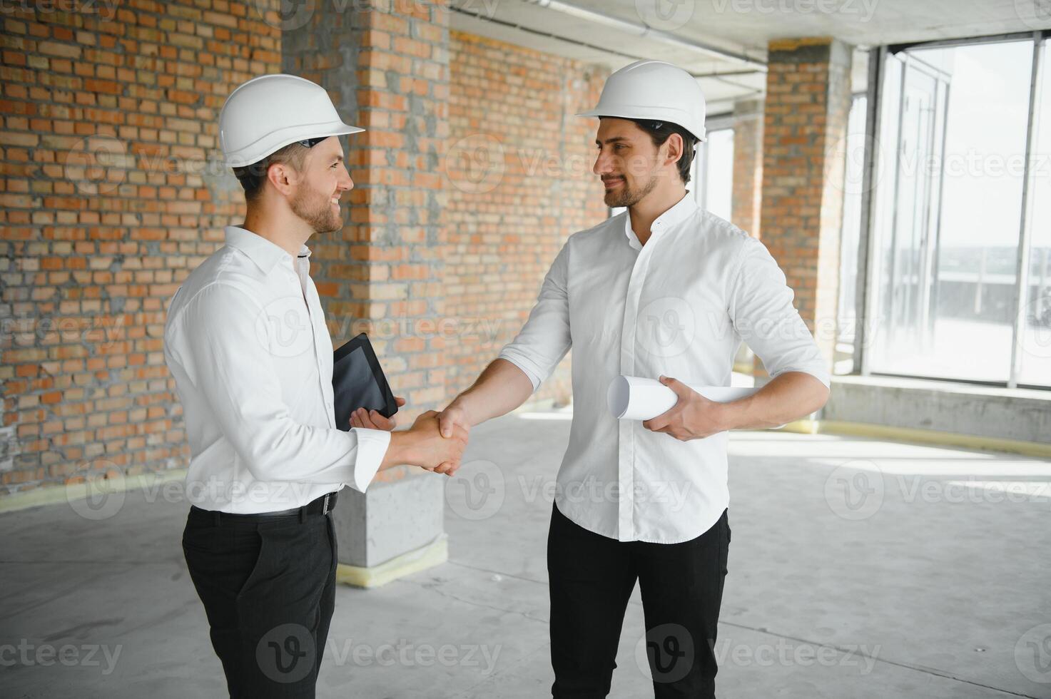 A front view of two smart architects with white helmets reviewing blueprints at a construction site on a bright sunny day photo