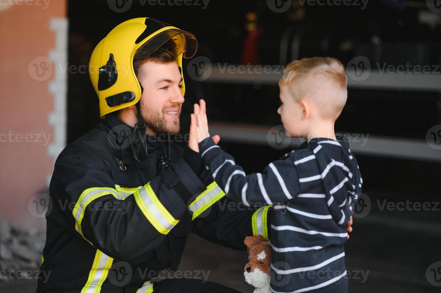 Portrait of rescued little boy with firefighter man standing near fire truck. Firefighter in fire fighting operation. photo