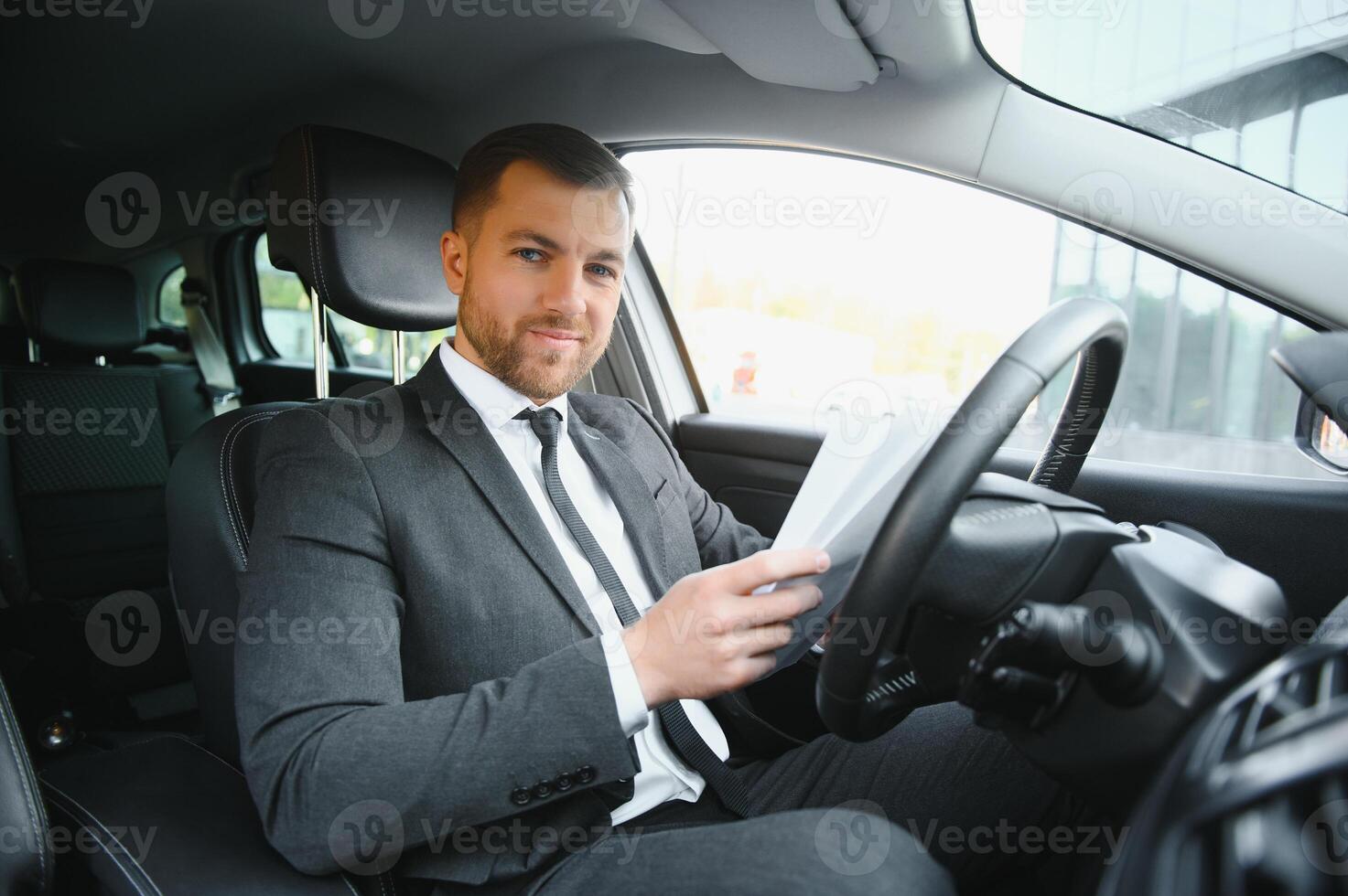 Man of style and status. Handsome young man in full suit smiling while driving a car photo