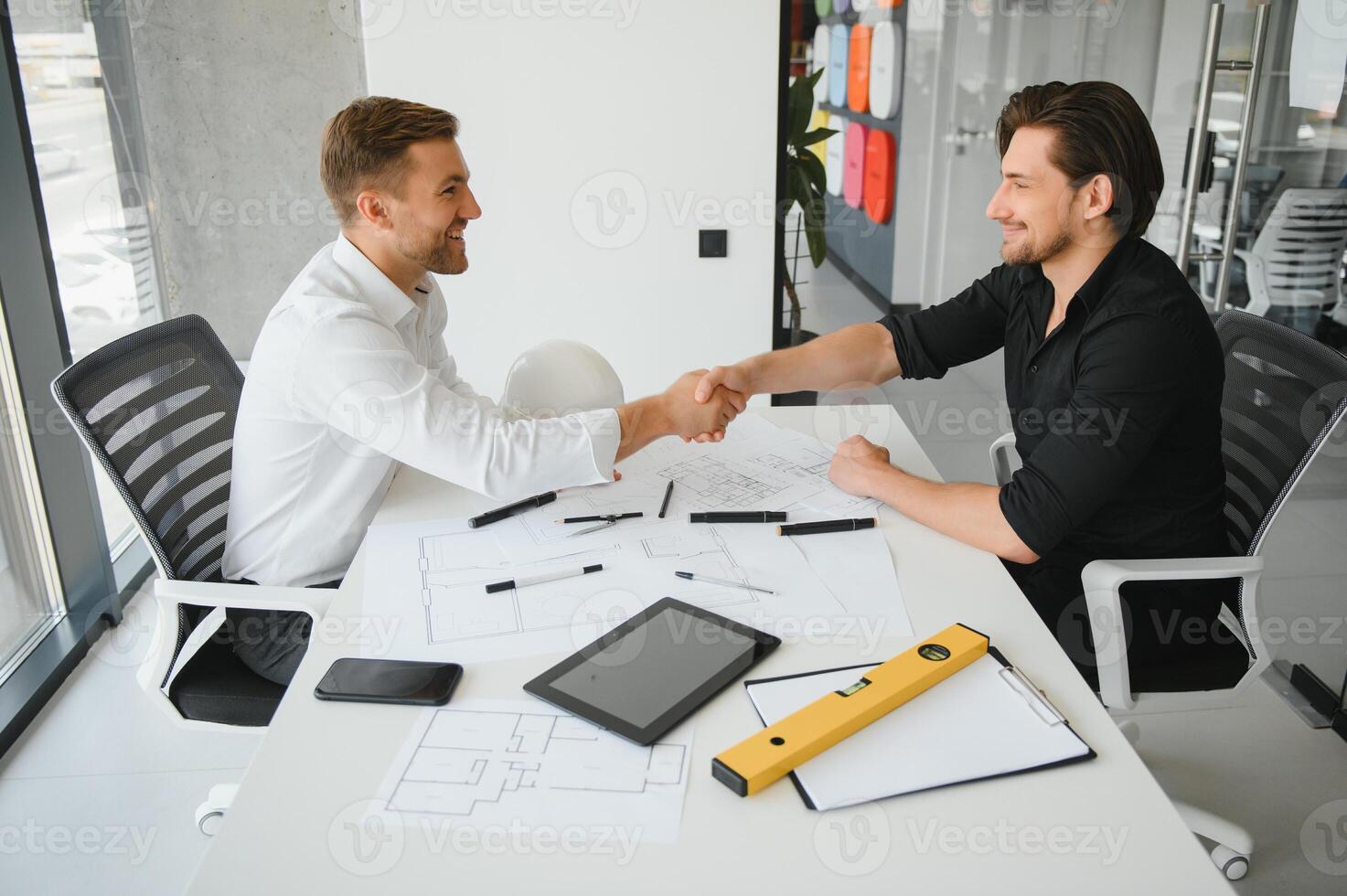 Two young architects with blueprints of a house standing in office, talking. photo