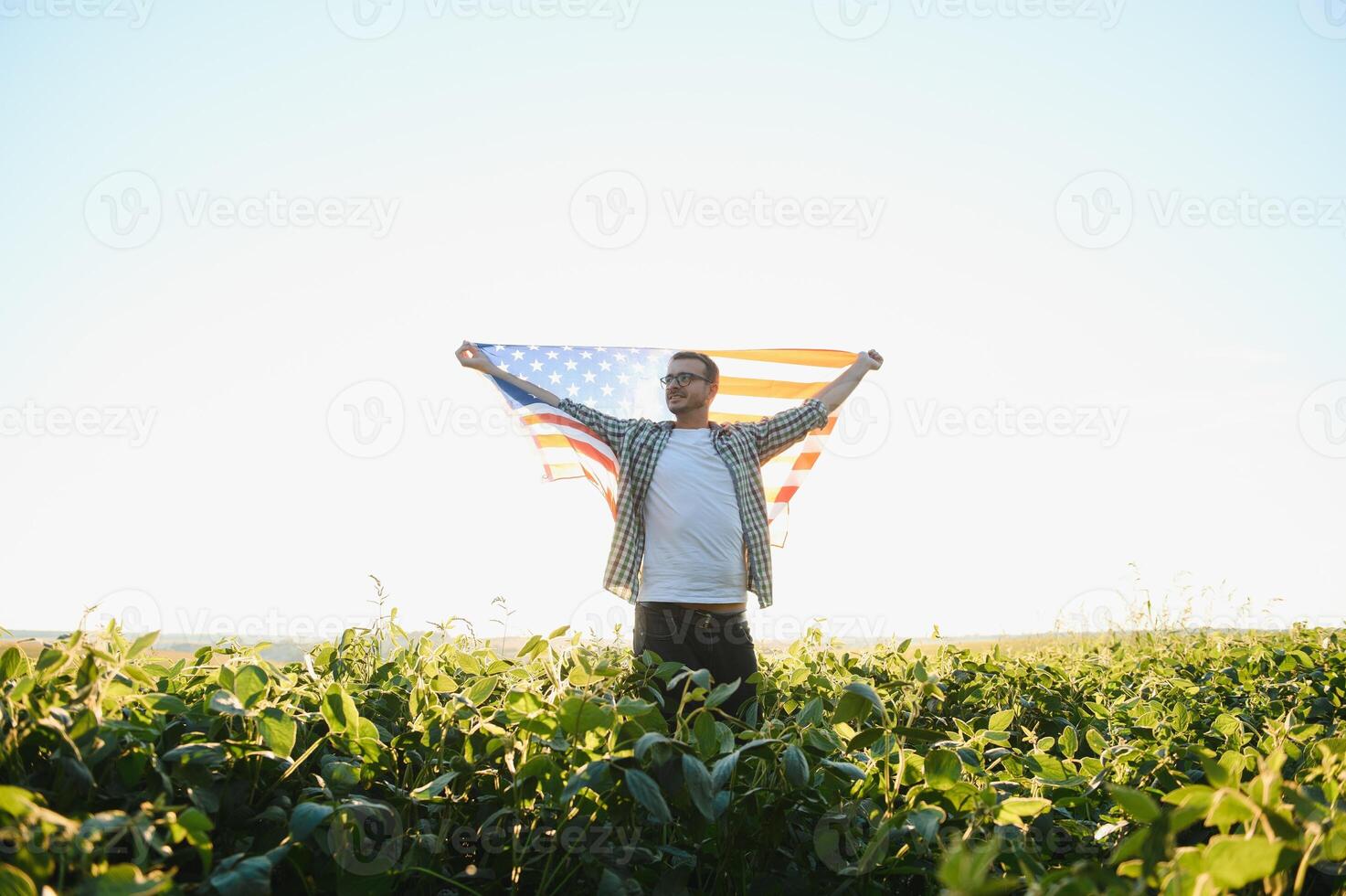 A young farmer stands with a USA flag in a soybean field. The concept of the US agricultural industry. photo