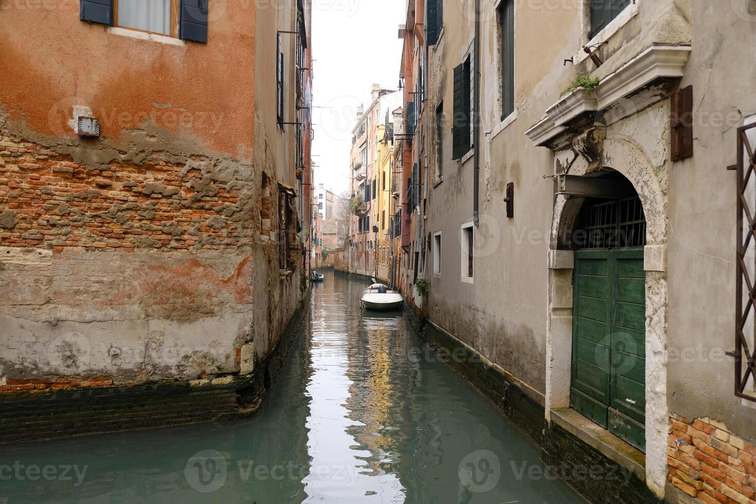 Typical narrow streets and canals between colorful and shabby houses in Venice, Italy. Historical architecture in Venice, parked boats on the canals. photo