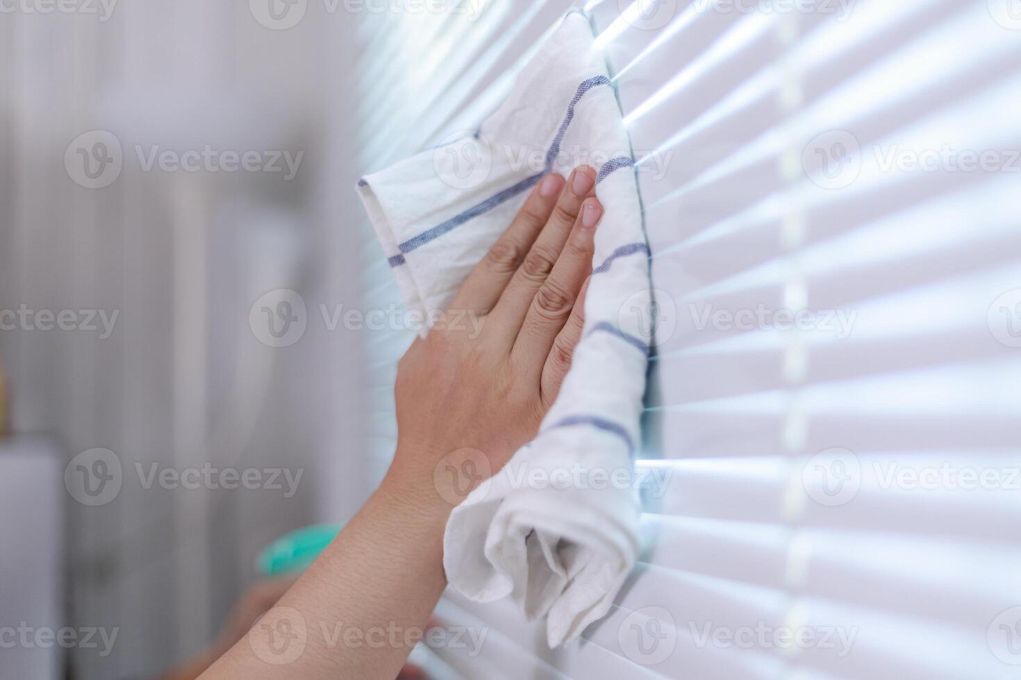 Hands of the woman uses fabric and water spray to clean the window blind photo