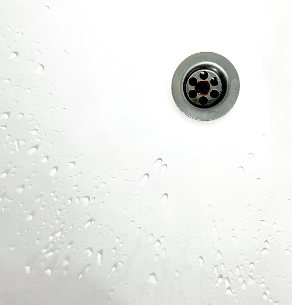 Wet white colored ceramic sink surface on the inside with stainless steel water hole and water drop stains. photo