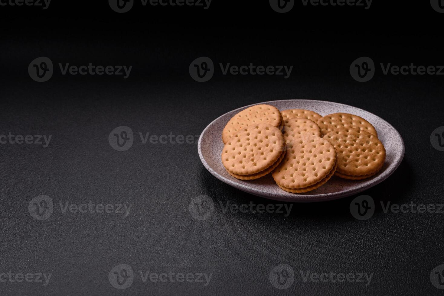 Round dotted snack snack cookies with cream on a dark concrete background photo