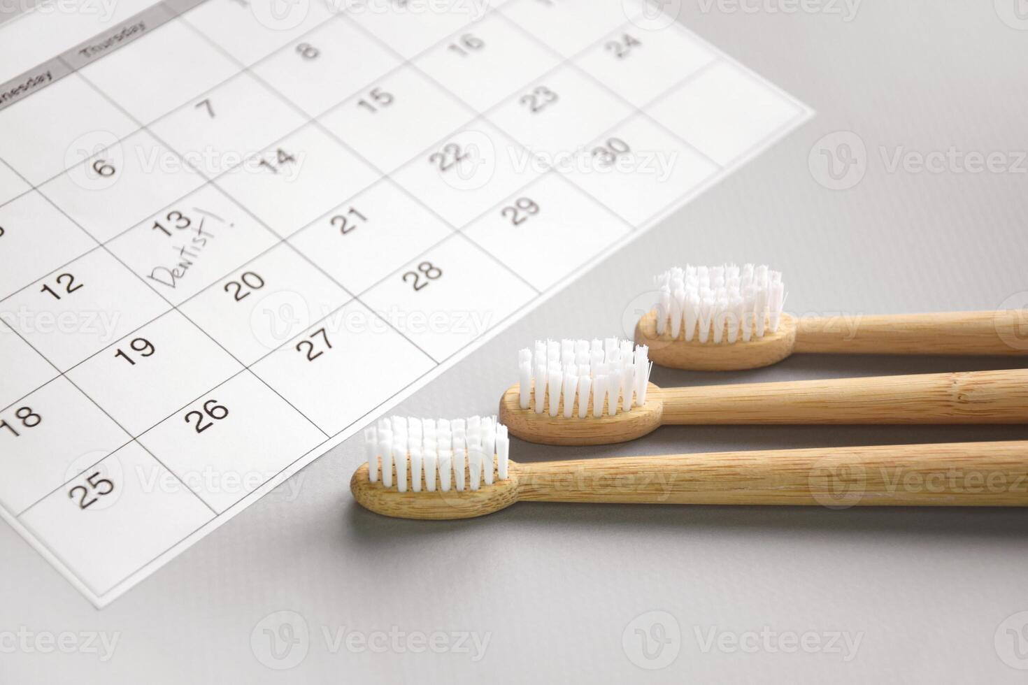 On a light gray background, there is a calendar with a dentist's note and toothbrushes. photo