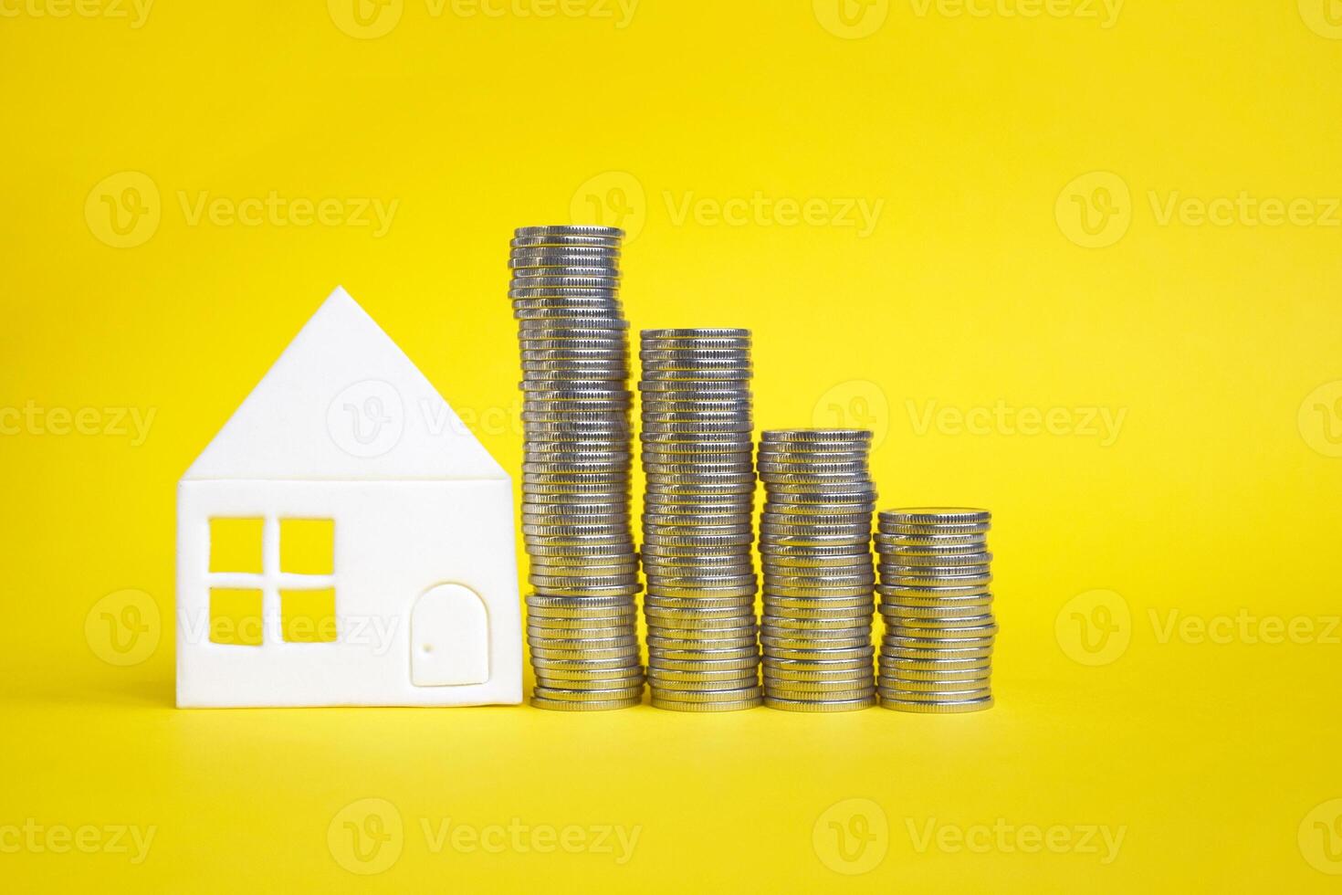 Several columns of coins and a small white paper house. photo