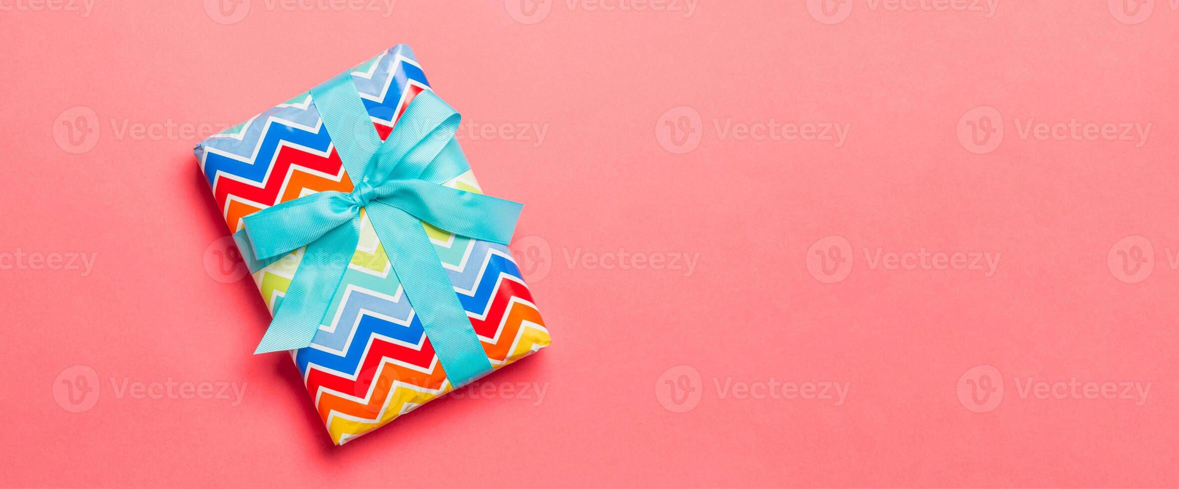 wrapped Christmas or other holiday handmade present in paper with blue ribbon on living coral background. Present box, decoration of gift on colored table, top view with copy space photo