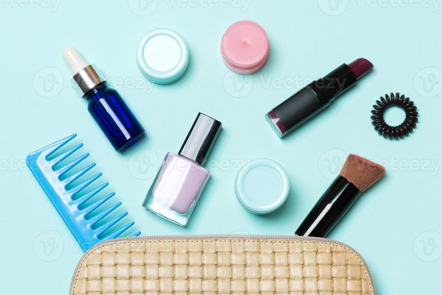 Top view of set of make up and skin care products spilling out of cosmetics bag on blue background. Beauty concept photo