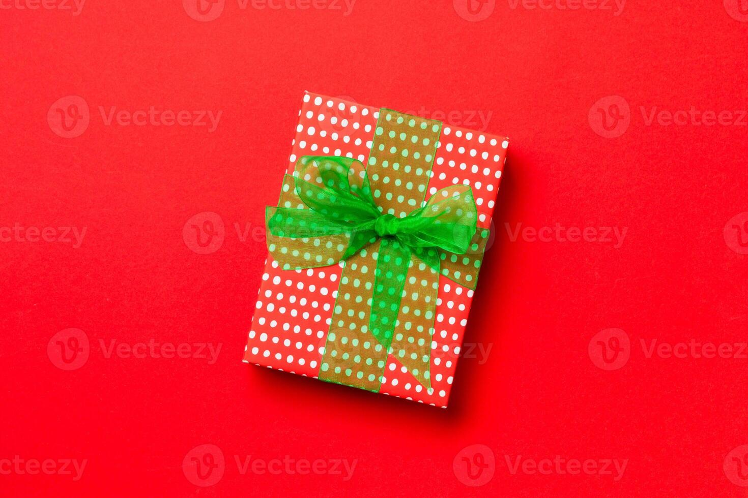 Gift box with green bow for Christmas or New Year day on red background, top view with copy space photo