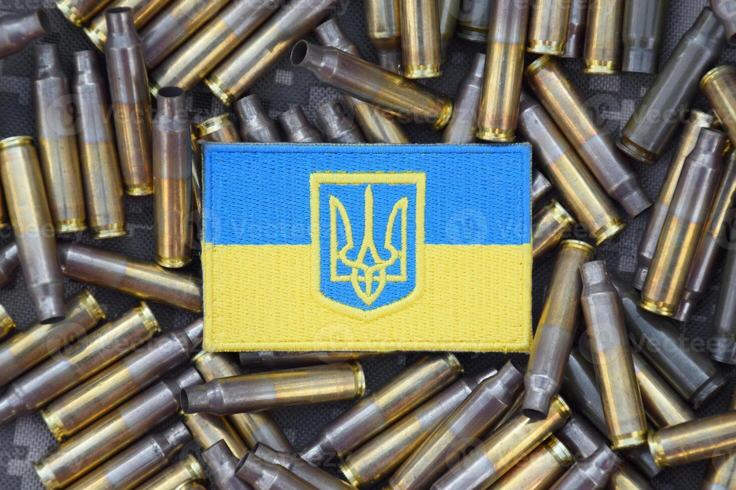 Ukrainian national flag with the coat of arms on the background of military camouflage surrounded by shells. photo