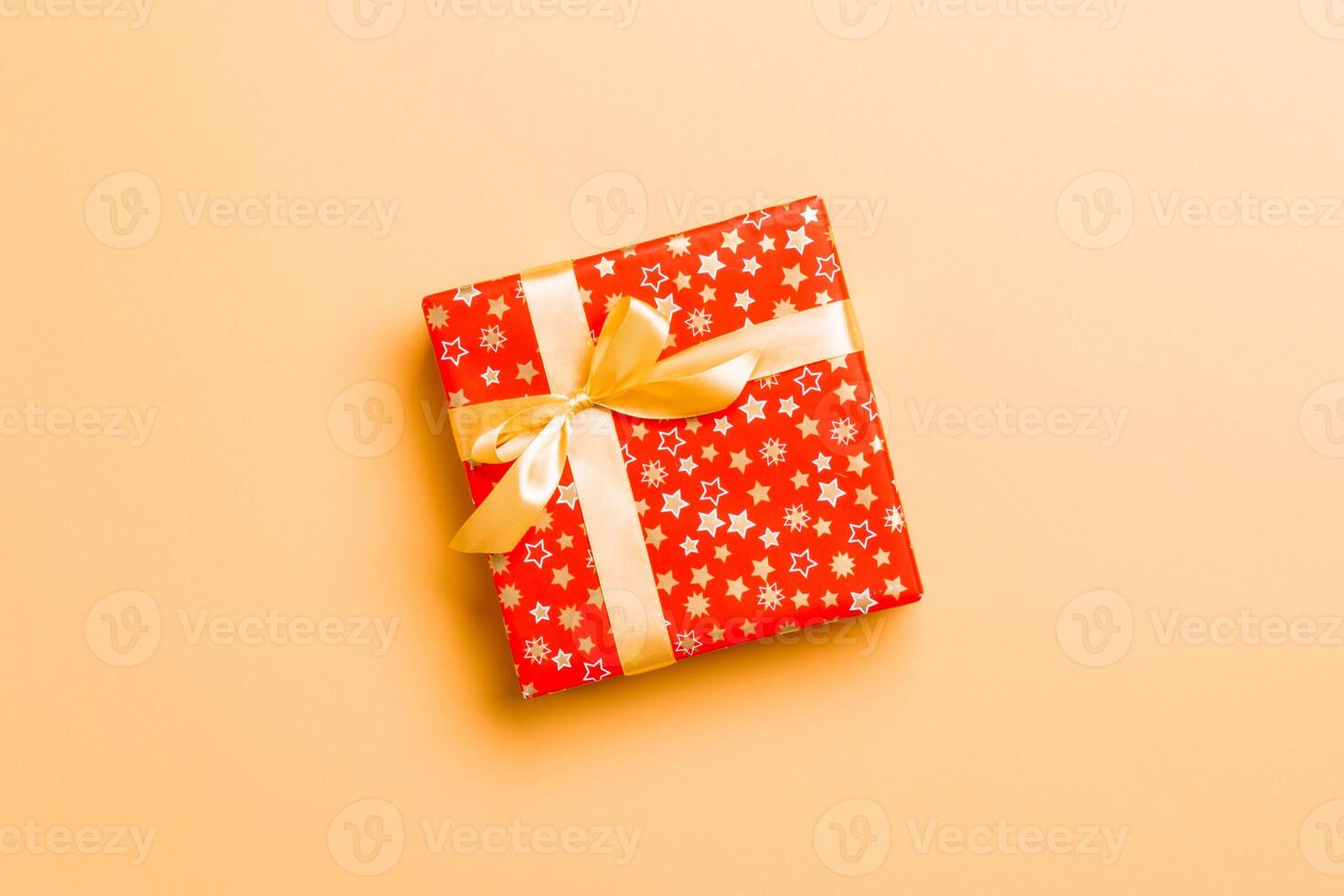 wrapped Christmas or other holiday handmade present in paper with Gold ribbon on orange background. Present box, decoration of gift on colored table, top view with copy space photo