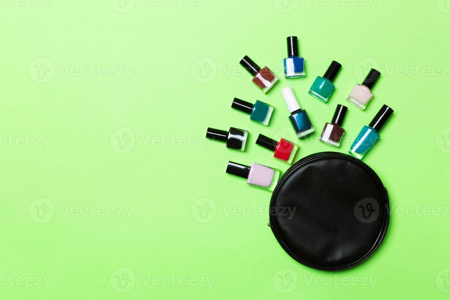 Top view of the set of nail polishes and bright gel varnishes fallen out of cosmetics bag with copy space on green background. Trendy nail concept photo