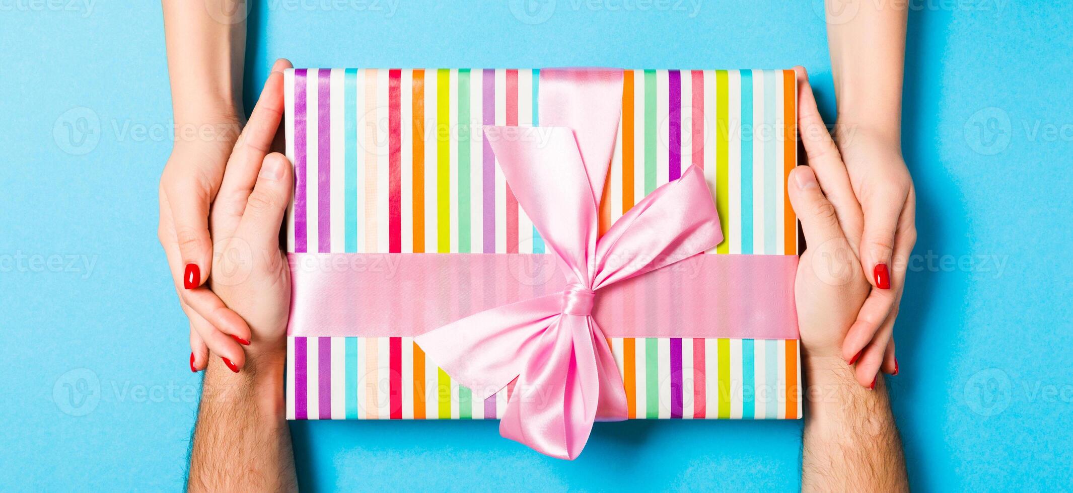 Top view of a man and a woman holding a gift box on colorful background. Love and relationship concept. Close up photo