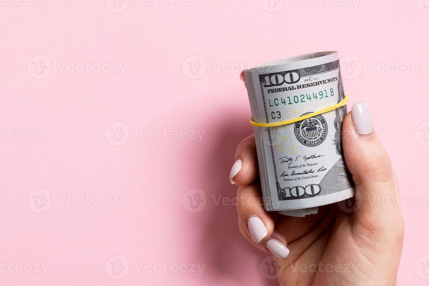 Top view of female hand holding a pack of rolled money on colorful background. One hundred dollars. Business concept with empty space for your design. Charity and tips concept photo