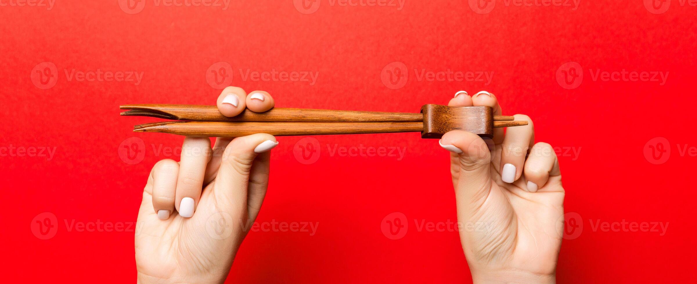 Crop image of two female hands holding chopsticks on red background. Ready to eat concept with copy space photo