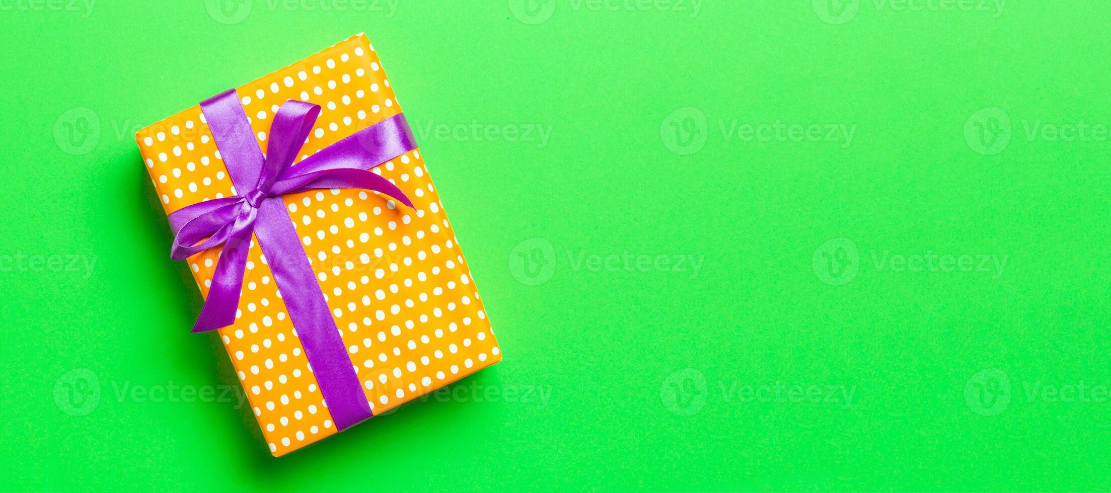 Top view Christmas present box with purple bow on green background with copy space photo