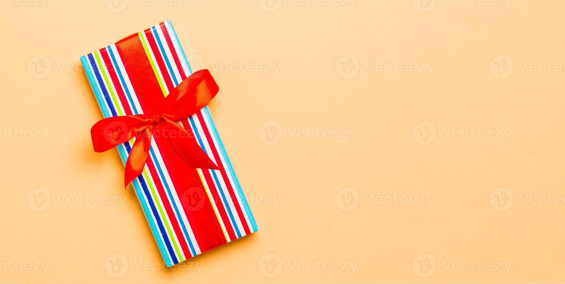 Top view Christmas present box with red bow on orange background with copy space photo