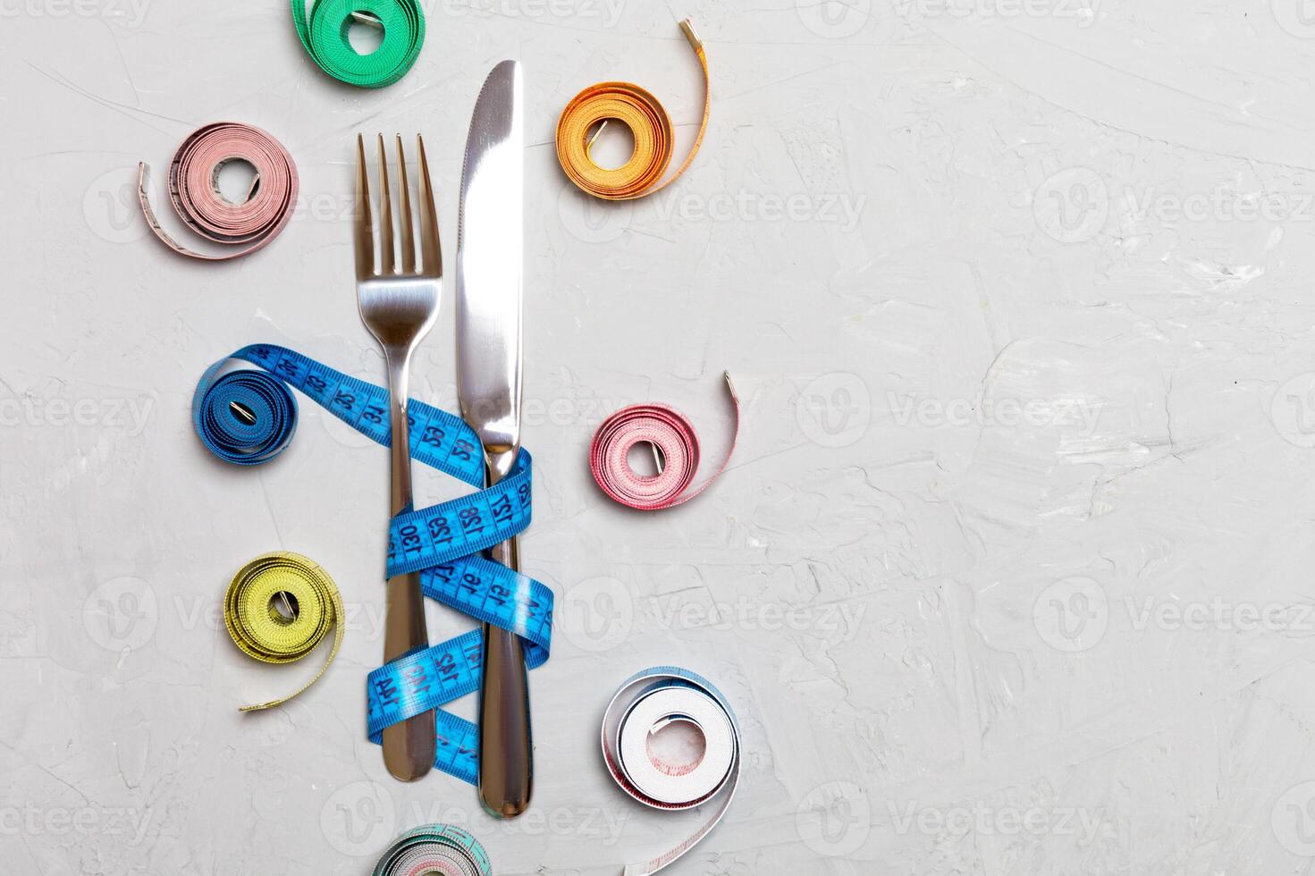Composition of colored measuring tapes, fork and knife on cement background with empty space for your design. Overweight concept photo