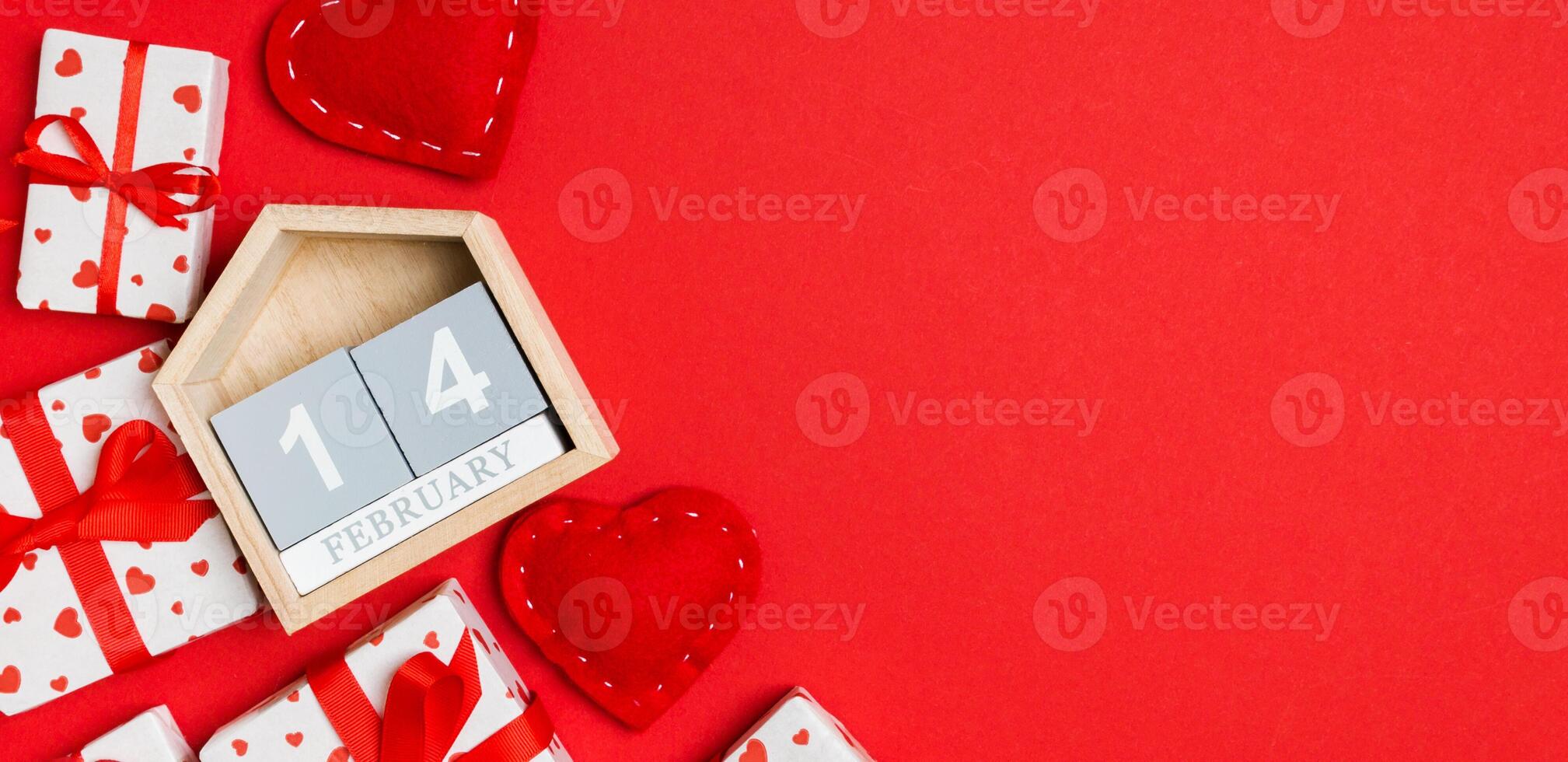 Top view of gift boxes, wooden calendar and red textile hearts on colorful background. The fourteenth of february. St Valentine's day concept with copy space photo